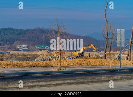 Daejeonn, Südkorea, 25. Dezember 2019: Unbekannter Mann in blauem Hardhat, der vor einem Baggerlader steht und Schmutz und Müll auf der Baustelle bewegt. Stockfoto