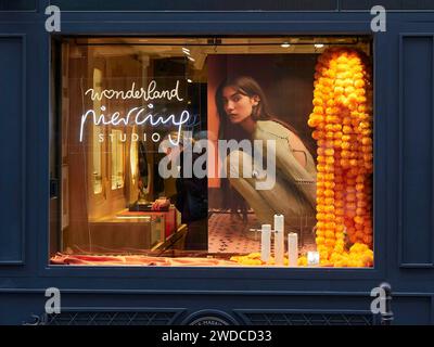 Ein Schaufenster eines Modegeschäfts, beleuchtet mit warmen Lichtern und eine Werbung mit einer Frau darauf. Paris Stockfoto