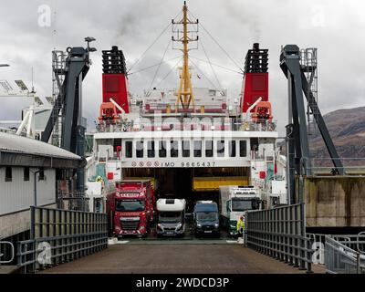 Lkw und Autos warten auf eine große Fähre in einem Hafen mit einer bergigen Landschaft im Hintergrund, Stornoway Fährhafen. Ankunft des Stockfoto