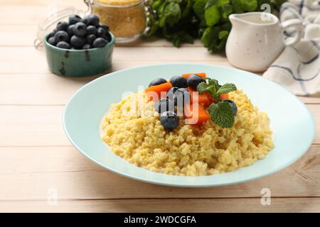 Teller mit leckerem Hirsebrei, Heidelbeeren, Kürbis und Minze auf hellem Holztisch Stockfoto