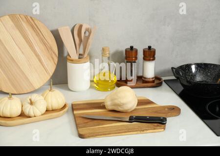 Schneidebretter aus Holz, andere Kochutensilien und Kürbisse auf weißer Arbeitsplatte in der Küche Stockfoto