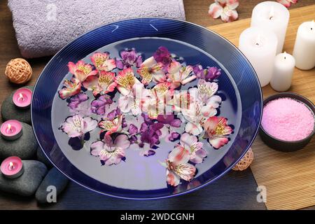 Schüssel mit Wasser mit Blumen, Kerzen, Steinen und Handtuch auf Holztisch. Spa-Behandlung Stockfoto