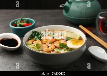 Köstliche Ramen mit Garnelen und Ei in Schüssel serviert auf grauem Tisch. Nudelsuppe Stockfoto