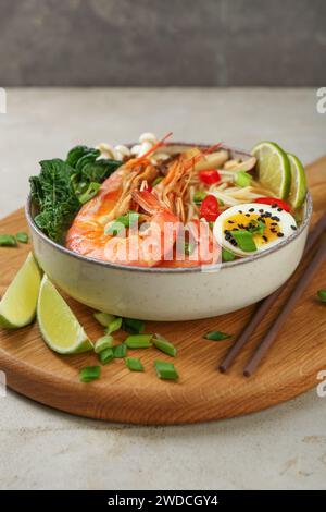 Köstliche Ramen mit Garnelen, Ei in der Schüssel und Stäbchen auf einem hellen, strukturierten Tisch. Nudelsuppe Stockfoto