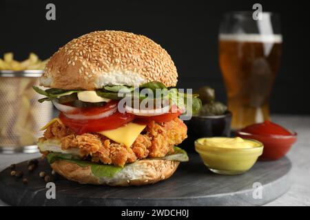 Leckerer Burger mit knusprigem Hähnchenpastete und Saucen auf grauem Tisch, Nahaufnahme Stockfoto