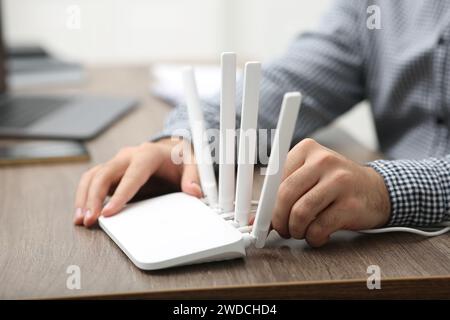 Mann, der Kabel in den WLAN-Router an einem Holztisch drinnen steckt, Nahaufnahme Stockfoto