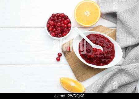 Leckere Preiselbeersauce in Schüssel, frische Beeren und Orangenscheiben auf weißem Holztisch, flach gelegt. Leerzeichen für Text Stockfoto