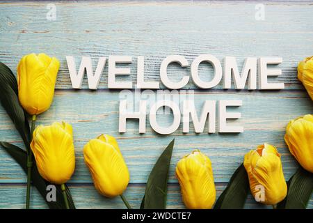 Willkommen-Haus-Alphabet mit gelber Tulpenblüte auf hölzernem Hintergrund Stockfoto