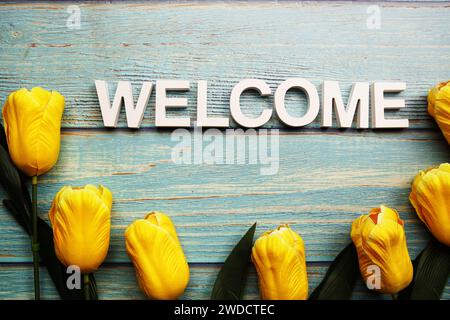 Begrüßungsalphabet mit gelber Tulpenblüte auf hölzernem Hintergrund Stockfoto