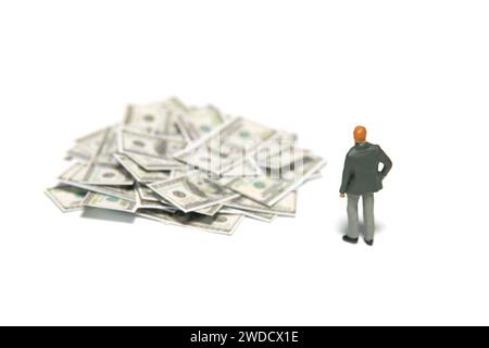 Miniatur-Kleinkinder-Spielfiguren-Fotografie. Anlageberatungskonzept. Ein Geschäftsmann, der auf Papier Bargeldhaufen sucht. Isoliert auf weißem Hintergrund. Stockfoto