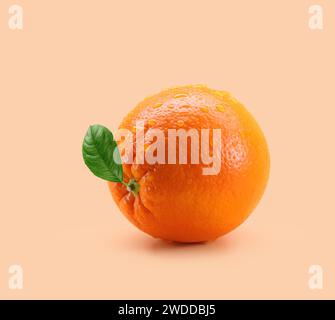 Orange mit Blatt und Tropfen auf hellorangem Hintergrund Stockfoto