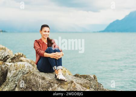 Schöne brünette Frau, die am See ruht und braune Lederjacke trägt Stockfoto