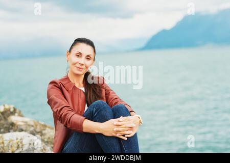 Schöne brünette Frau, die am See ruht und braune Lederjacke trägt Stockfoto