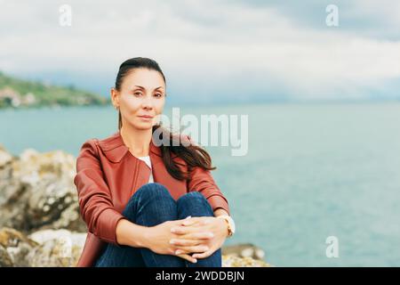 Schöne brünette Frau, die am See ruht und braune Lederjacke trägt Stockfoto