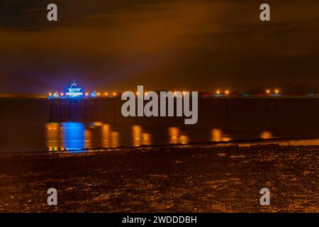 Die farbigen Lichter am Pier spiegeln sich auf das Meer und den Schlamm Stockfoto