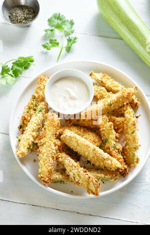 Gebackene knusprige Zucchini-Pommes mit Dippsoße auf Teller auf hellem Holzhintergrund. Stockfoto