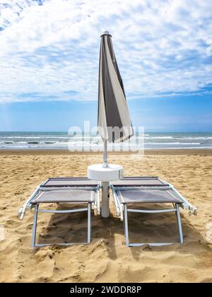 Zwei Liegen und ein Sonnenschirm geschlossen vor dem Meer am Ende des Sommers an einem einsamen Strand. Stockfoto