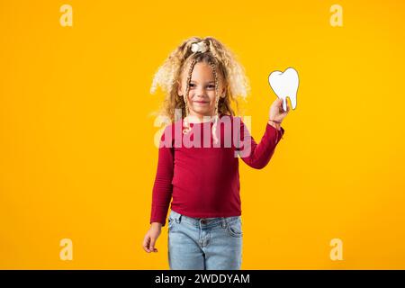 Ein Mädchen, das einen Zahn aus Papier hält, der Mundgesundheit symbolisiert. Zahnärztliches Gesundheitskonzept Stockfoto