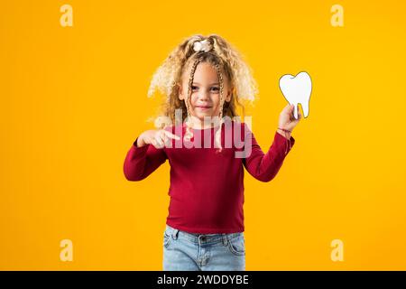 Ein Mädchen, das einen Zahn aus Papier hält, der Mundgesundheit symbolisiert. Zahnärztliches Gesundheitskonzept Stockfoto