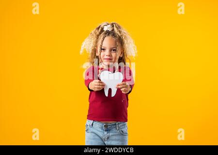 Ein Mädchen, das einen Zahn aus Papier hält, der Mundgesundheit symbolisiert. Zahnärztliches Gesundheitskonzept Stockfoto