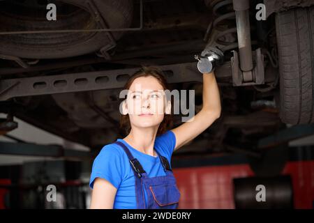 Eine hübsche Frau steht unter einem Wagen, der auf einem Aufzug hochgefahren ist Stockfoto