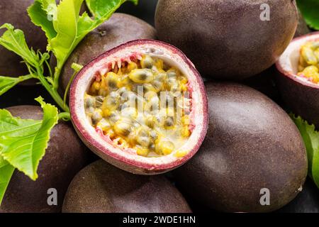 Reife Passionsfrüchte mit Passionsfruchtsamen und Passionsfruchtsblättern auf einem grauen Steintisch. Schöne exotische Frucht Hintergrund für Ihre Projekte. Stockfoto