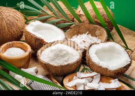 Frisch geöffnete Kokosnüsse zusammen mit Kokosscheiben, Flocken und Kokosblättern auf einem Holztisch. Schöner Hintergrund für Ihre Projekte. Stockfoto