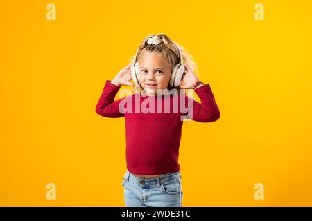 Fröhliches Kindermädchen mit Kopfhörern, in Musik verloren, ausdrucksvoll tanzen – bezauberndes Bild in einem Moment der reinen Freude. Stockfoto