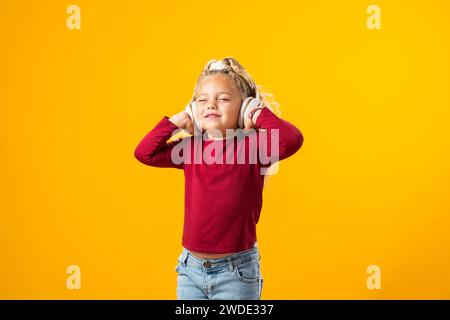 Fröhliches Kindermädchen mit Kopfhörern, in Musik verloren, ausdrucksvoll tanzen – bezauberndes Bild in einem Moment der reinen Freude. Stockfoto