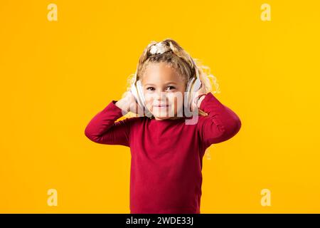 Fröhliches Kindermädchen mit Kopfhörern, in Musik verloren, ausdrucksvoll tanzen – bezauberndes Bild in einem Moment der reinen Freude. Stockfoto