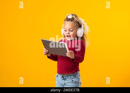 Fesselndes Porträt eines fröhlichen Jungen mit Kopfhörern und Tablet, eingetaucht in Videospielabenteuer. Freizeit- und Gadget-sucht-Konzept Stockfoto