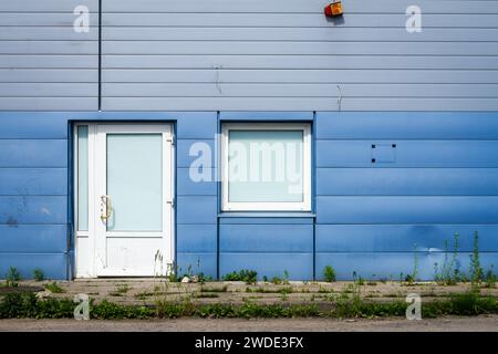 Details der blauen Fassade aus Aluminiumplatten mit Türen und Fenstern am Industriebau Stockfoto