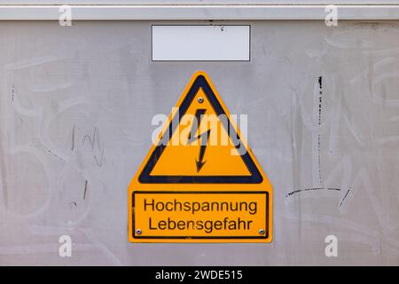 Gelbes Schild mit Warnung Hochspannungsgefahr auf Schaltkasten mit deutschem Text Stockfoto