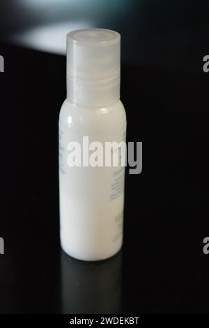 Damenkosmetik, kleine weiße Flasche Hautpflegecreme auf schwarzem Hochglanzhintergrund. Stockfoto