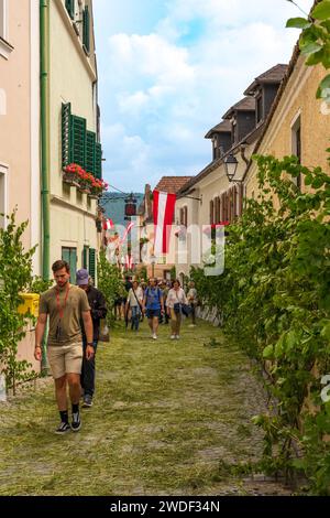 Dürnstein, Niederösterreich – AT – 8. Juni 2023 vertikales Bild von Touristen, die auf einer der malerischen Steinstraßen Dürnsteins zu Corpus C gehen Stockfoto