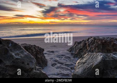 Lebendiger Sonnenaufgang am Strand mit auffälligen Wolken und felsigem Vordergrund, perfekt für Marketingkampagnen, Reiseblogs und künstlerische Inspirationen. Stockfoto