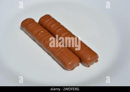 Süßigkeiten, Sticks mit Milchschokolade, Shortbread-Leber und Karamell auf einer weißen Glasplatte. Stockfoto