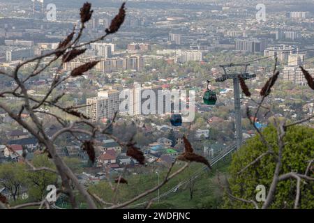 Luftbrücke zum Kok Tobe Hügel in Kasachstan. Seilbahn mit zwei Kabinen, vor dem Hintergrund der Stadt Almaty im Frühling. Touristenort, Stadt Landmar Stockfoto