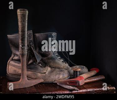 Alte Arbeitsstiefel aus Leder und Pickel-Axt auf einem Koffer-Stillleben Stockfoto