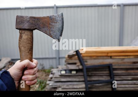 Mann mit Axt. Axt in der Hand. Ein starker Mann hält eine Axt in den Händen vor dem Hintergrund von Feuerholz. Selektiver Fokus, unscharfer Hintergrund Stockfoto