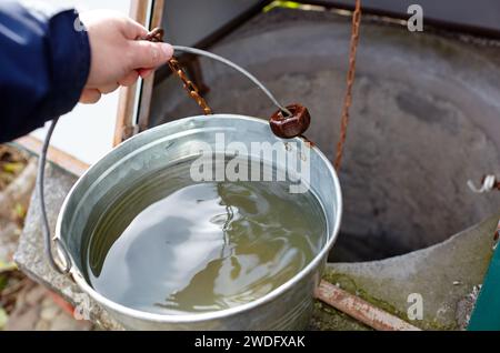 Man hält einen Metalleimer mit frischem Wasser. Wasser aus einem tiefen Brunnen in ländlicher Gegend Stockfoto