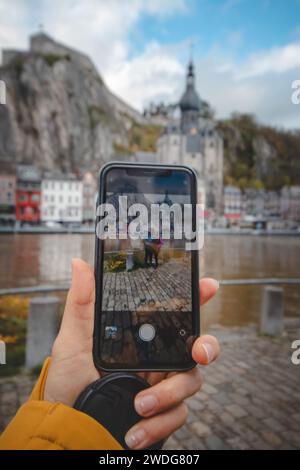 Verliebte Paare stehen am Ufer des Flusses La Mause vor der Wahrzeichen-Stadt Dinant, fotografiert mit einem Mobiltelefon. Tageslicht. Stockfoto