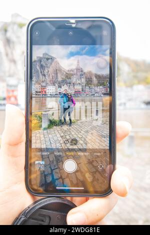 Verliebte Paare stehen am Ufer des Flusses La Mause vor der Wahrzeichen-Stadt Dinant, fotografiert mit einem Mobiltelefon. Tageslicht . Stockfoto