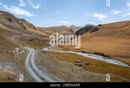 Straße, Strecke zwischen Hügeln mit gelbem Gras, der Fluss Kol Suu windet sich durch ein Bergtal, Provinz Naryn, Kirgisistan Stockfoto