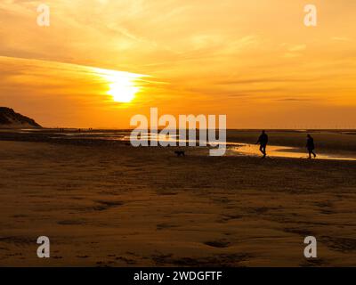 Ein Paar spaziert mit einem Hund bei Sonnenuntergang am Talacre Beach bei Ebbe, Talacre, Flintshire, Wales Stockfoto