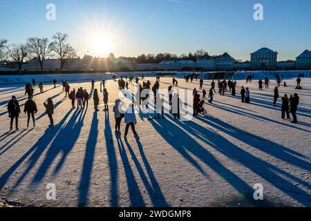 Wintervergnügen auf dem zugefrorenen Nymphenburger Kanal, München, Januar 2024 Deutschland, München, Januar 2024, Wintervergnügen am Nymphenburger Schlosskanal, Eislaufen und Spazierengehen, viele Münchner bummeln am Samstagnachmittag bei Minusgraden über den zugefrorenen Kanal oder laufen Schlittschuh, die tiefstehende Wintersonne wirft lange Schatten und taucht die Szene in ein warmes Gegenlicht, Temperaturen bei -8 Grad und Sonnenschein, Schloss Nymphenburg, Eisfläche noch tragfähig, Wettervorhersage für die nächsten Tage sagt stark steigende Temperaturen voraus, das Eis wird dann schnell b Stockfoto