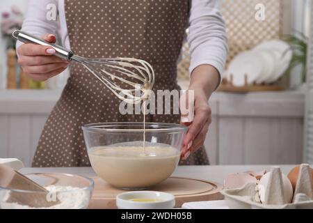 Frau, die Teig mit dem Schneebesen in der Schüssel am Tisch macht, Nahaufnahme Stockfoto