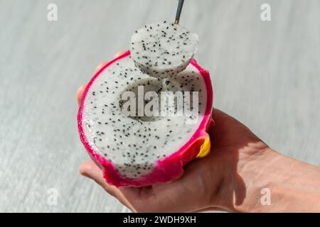 Der Mann hält einen Löffel mit der Hand, isst eine Drachenfrucht, zieht schön runde Stücke heraus, Fruchtscheiben Stockfoto