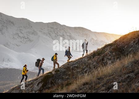 Gruppe von jungen aktiven Wanderern mit Rucksäcken geht bei Sonnenuntergang bergauf in die Berge Stockfoto