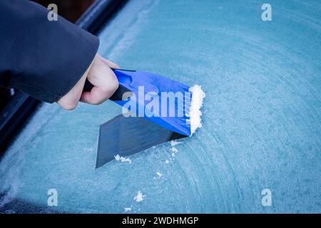 Eine Nahaufnahme eines Mannes, der an einem Wintertag Eis von der Windschutzscheibe des Autos kratzt Stockfoto